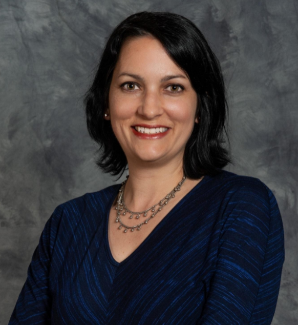 White woman in a black shirt in front of a grey background smiles